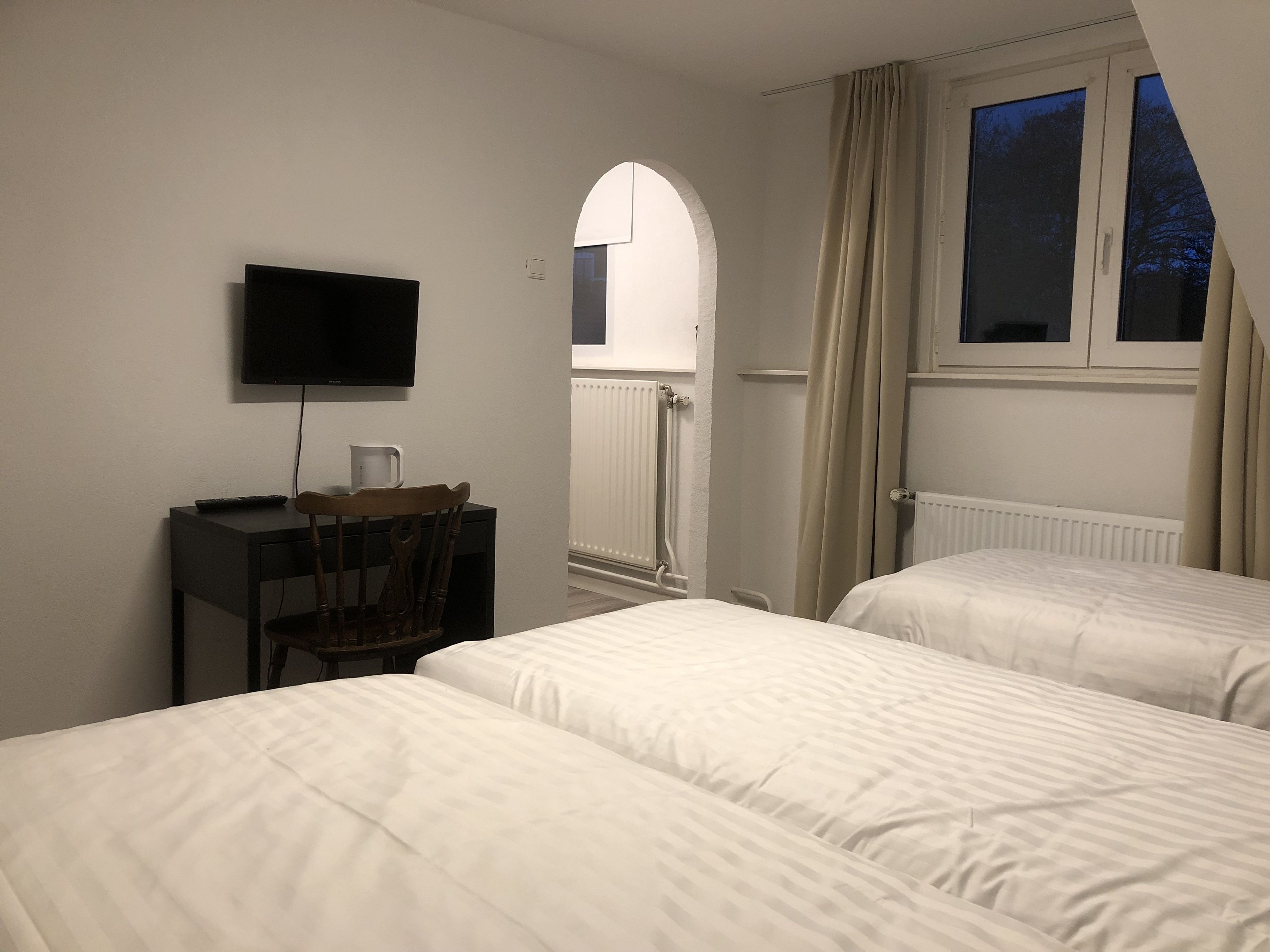A hotel room with two beds, a desk with a TV, a chair, and a window with curtains.
