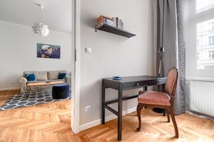 Um quarto com uma escrivaninha, uma cadeira, um sofá, uma estante de livros e um quadro.