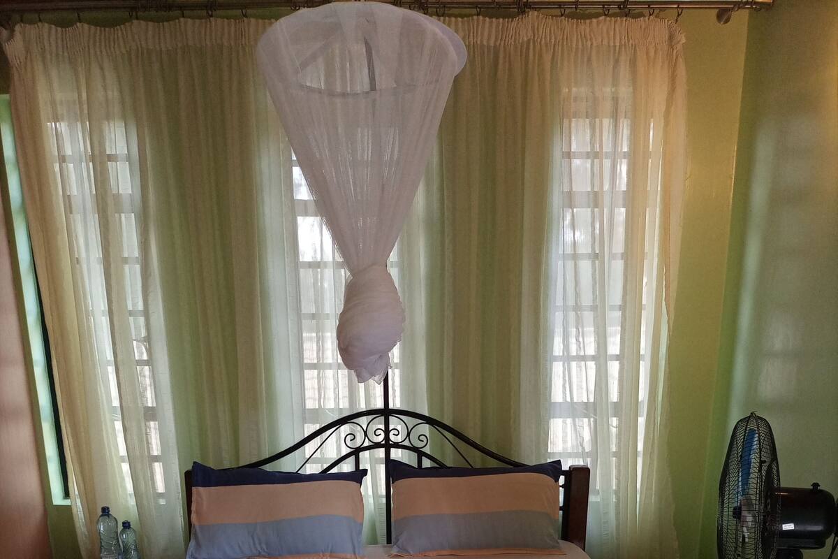 Un lit avec une couette rose, une moustiquaire et un ventilateur.