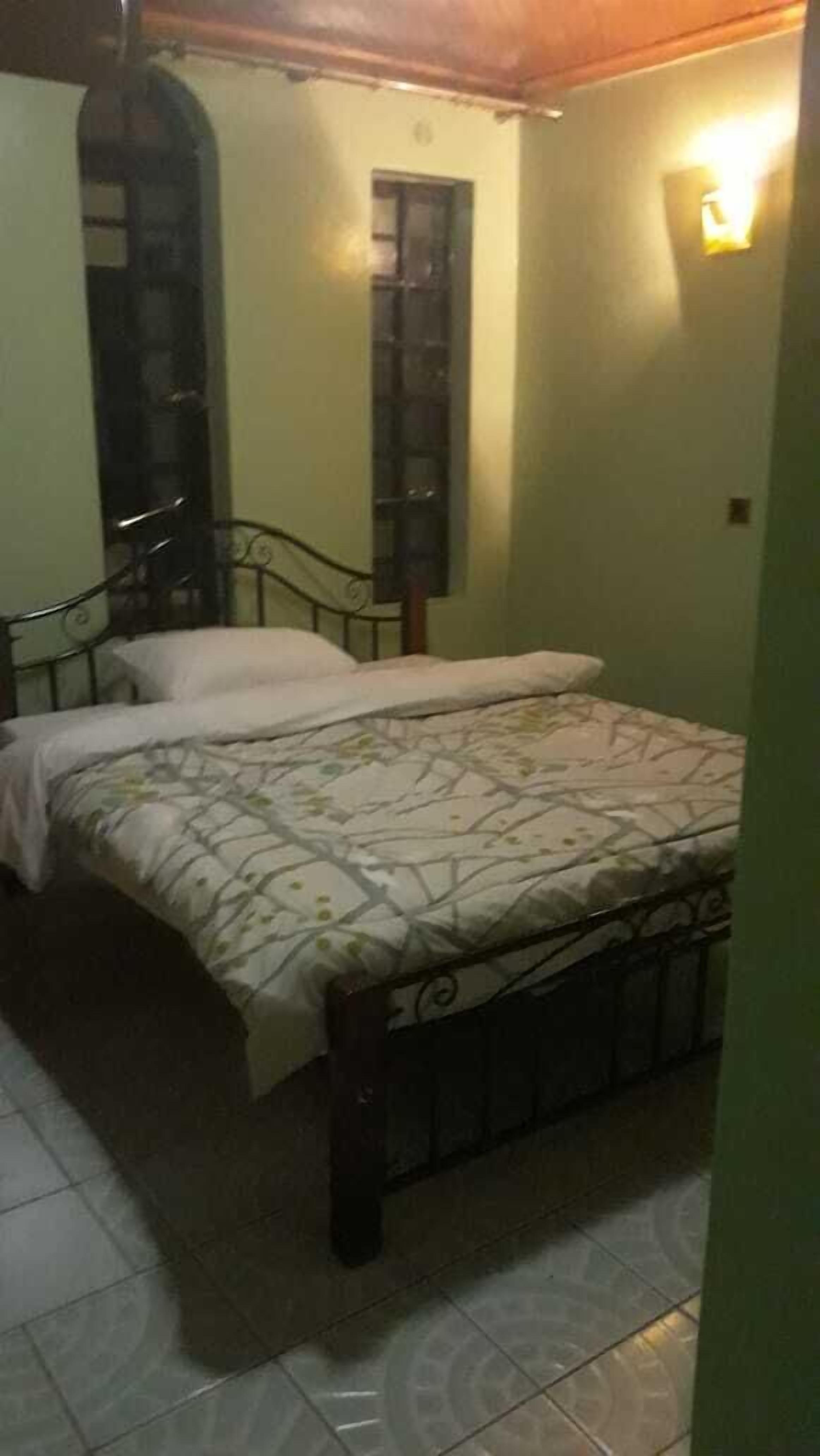 A bedroom with a bed, a window, and a wall-mounted light fixture.