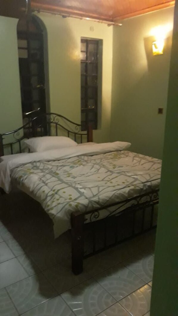 A bedroom with a bed, a window, and a wall-mounted light fixture.