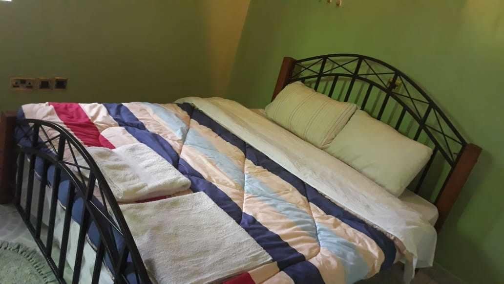 Un lit simple avec un cadre en métal, une couverture à rayures et un seul oreiller.