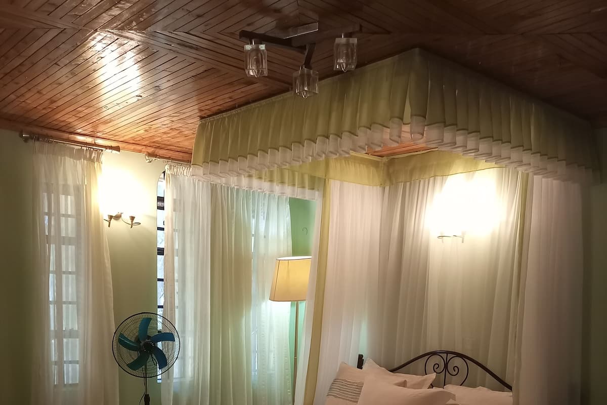 Une chambre à coucher avec un lit, un ventilateur sur pied et des rideaux.