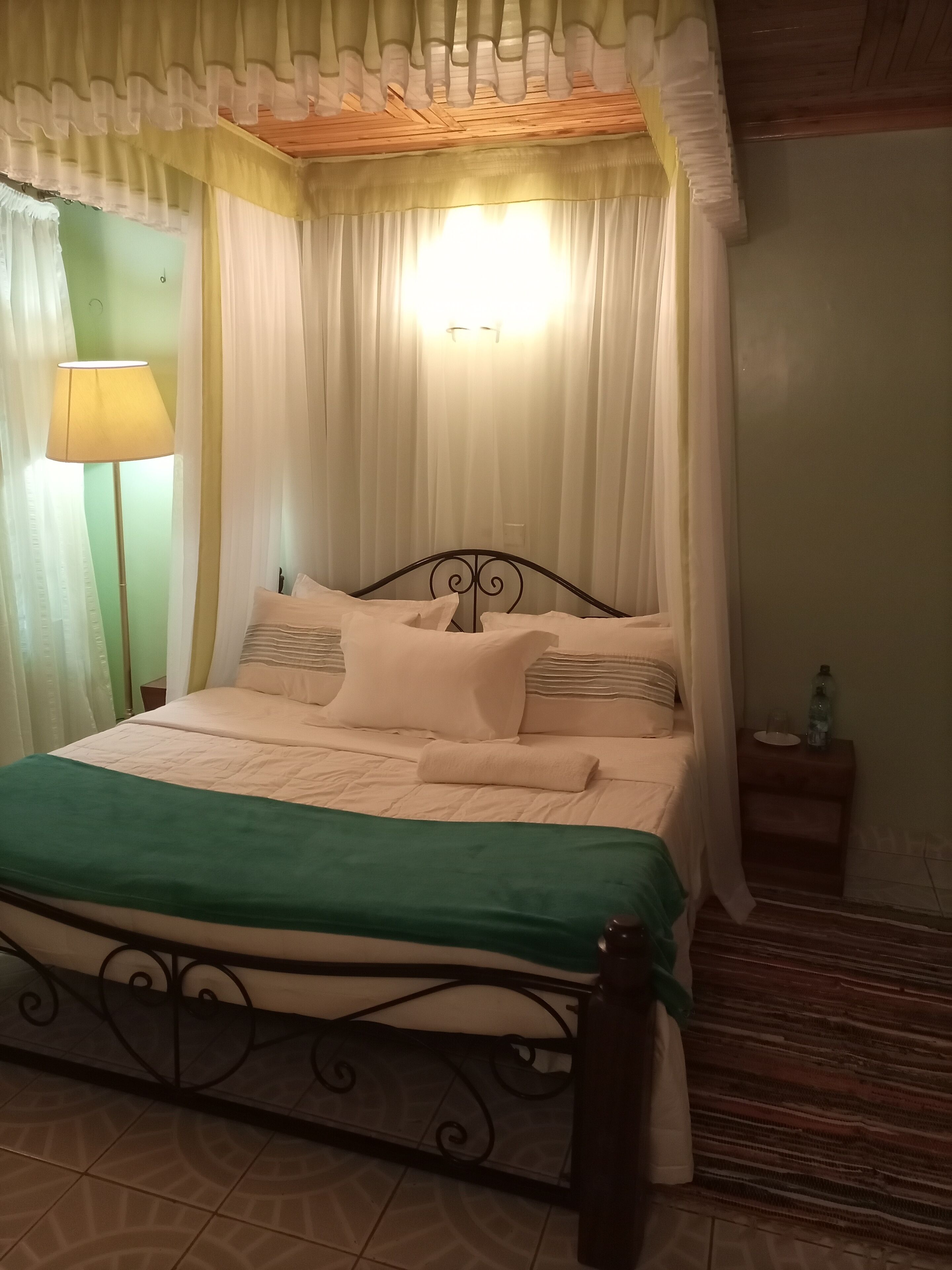 A neatly made bed with a green blanket, a bedside lamp, and a nightstand with a bottle and glass.