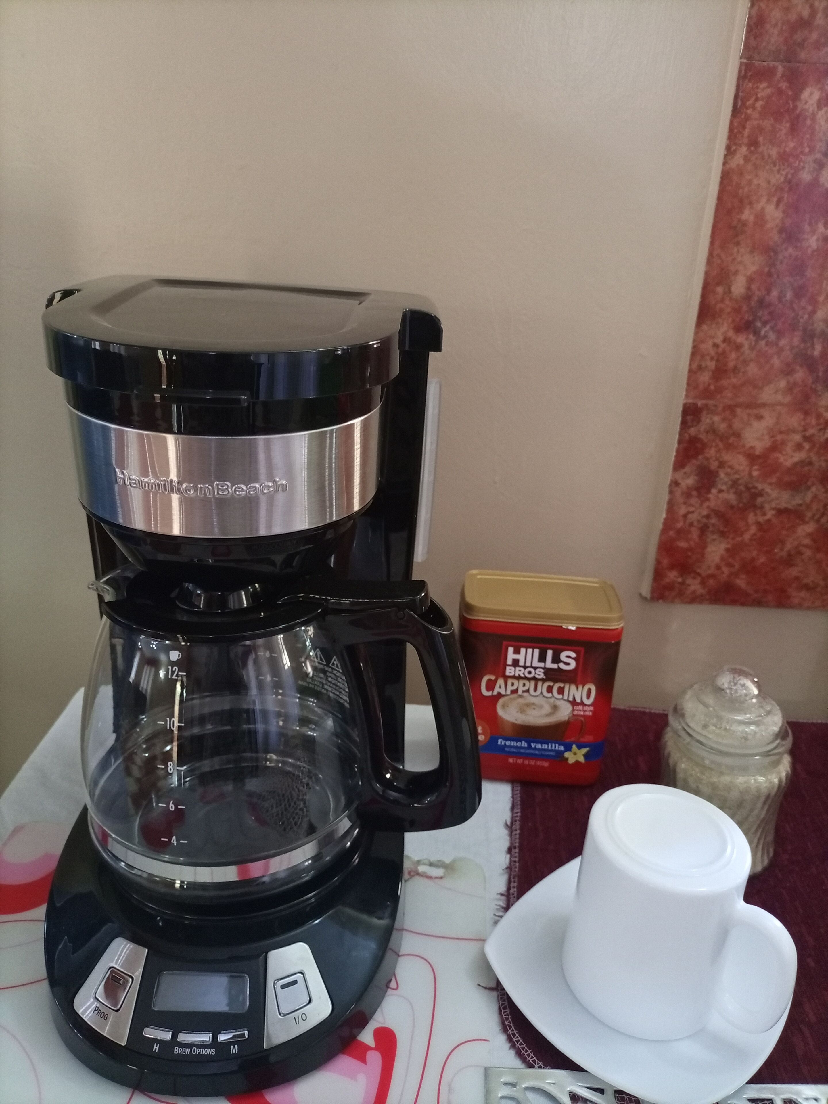 Een koffiezetapparaat met digitaal scherm, een houder voor koffiekapsules, een kop en een suikerpotje op een tafel.