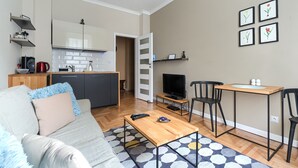 A compact living space with a sofa, coffee table, TV, and kitchenette. - MARGI Nell Apartament (Szczecin)