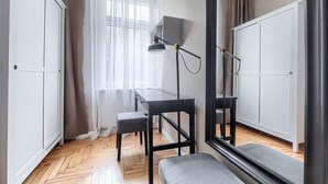 A room with a wooden floor, a desk with a lamp, a bench, and white wardrobes. - MARGI Nell Apartament (Szczecin)