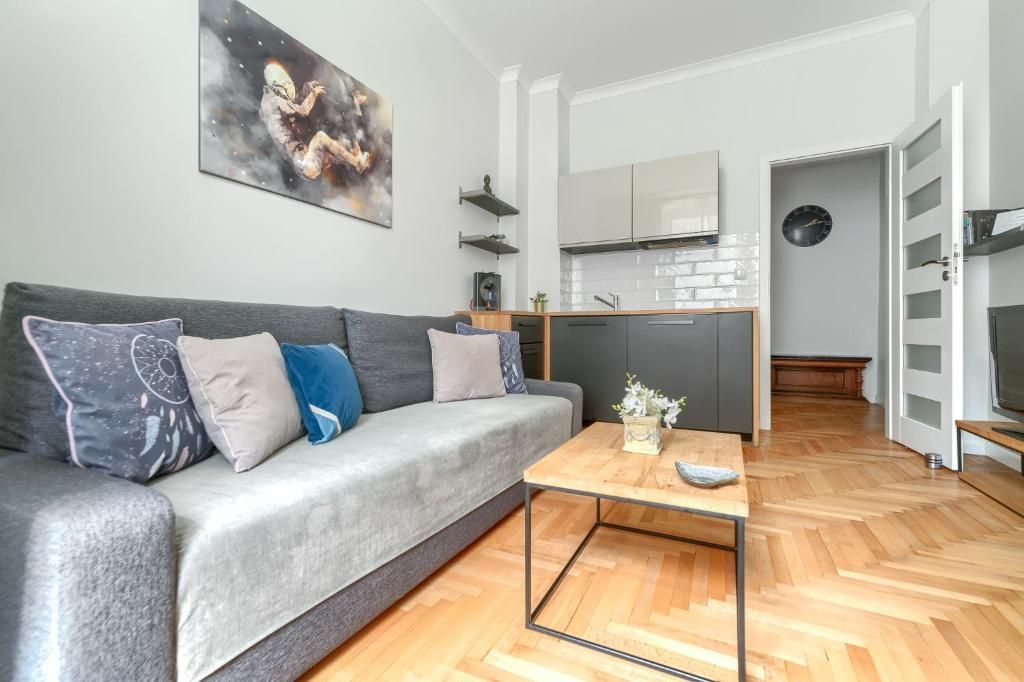 Una sala de estar moderna con un sofá gris, una mesa de centro de madera y una cocina al fondo.