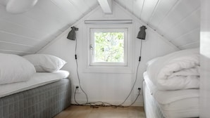 Un dormitorio pequeño estilo ático, con dos camas, una ventana y un ventilador de techo.