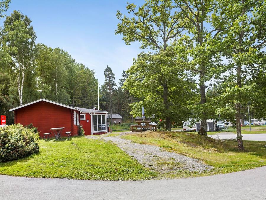 Une cabane rouge avec une table de pique-nique et un banc, entourée de verdure et d’arbres.