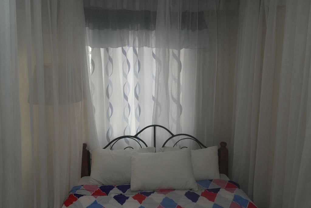 Un lit avec un cadre en métal et une literie blanche, recouvert de rideaux légers.