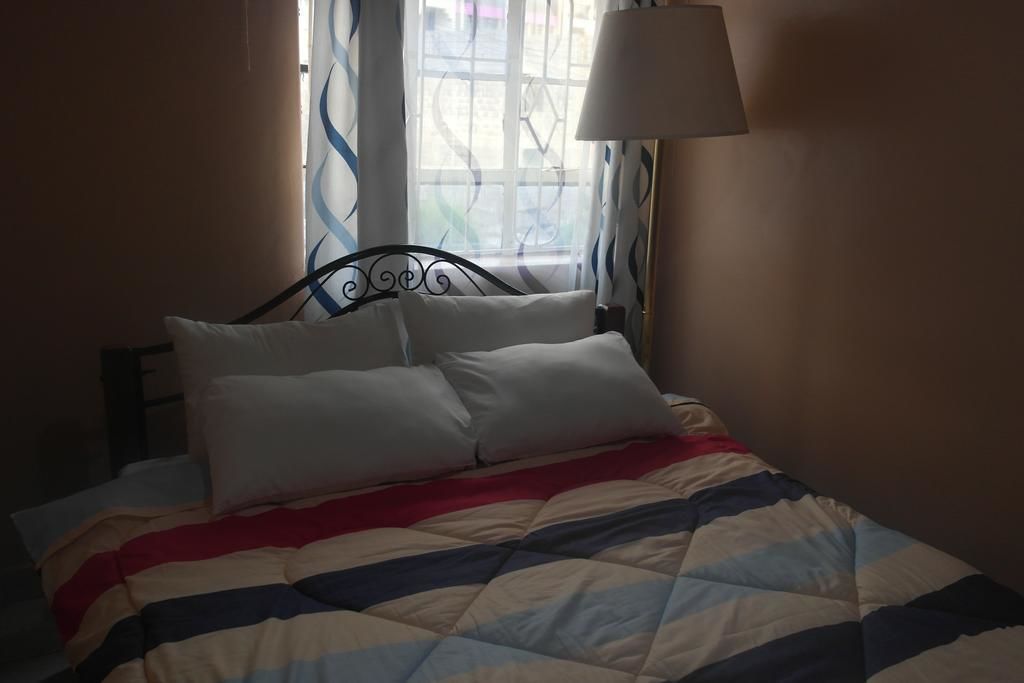 A bed with a striped quilt, a bedside lamp, and curtains.
