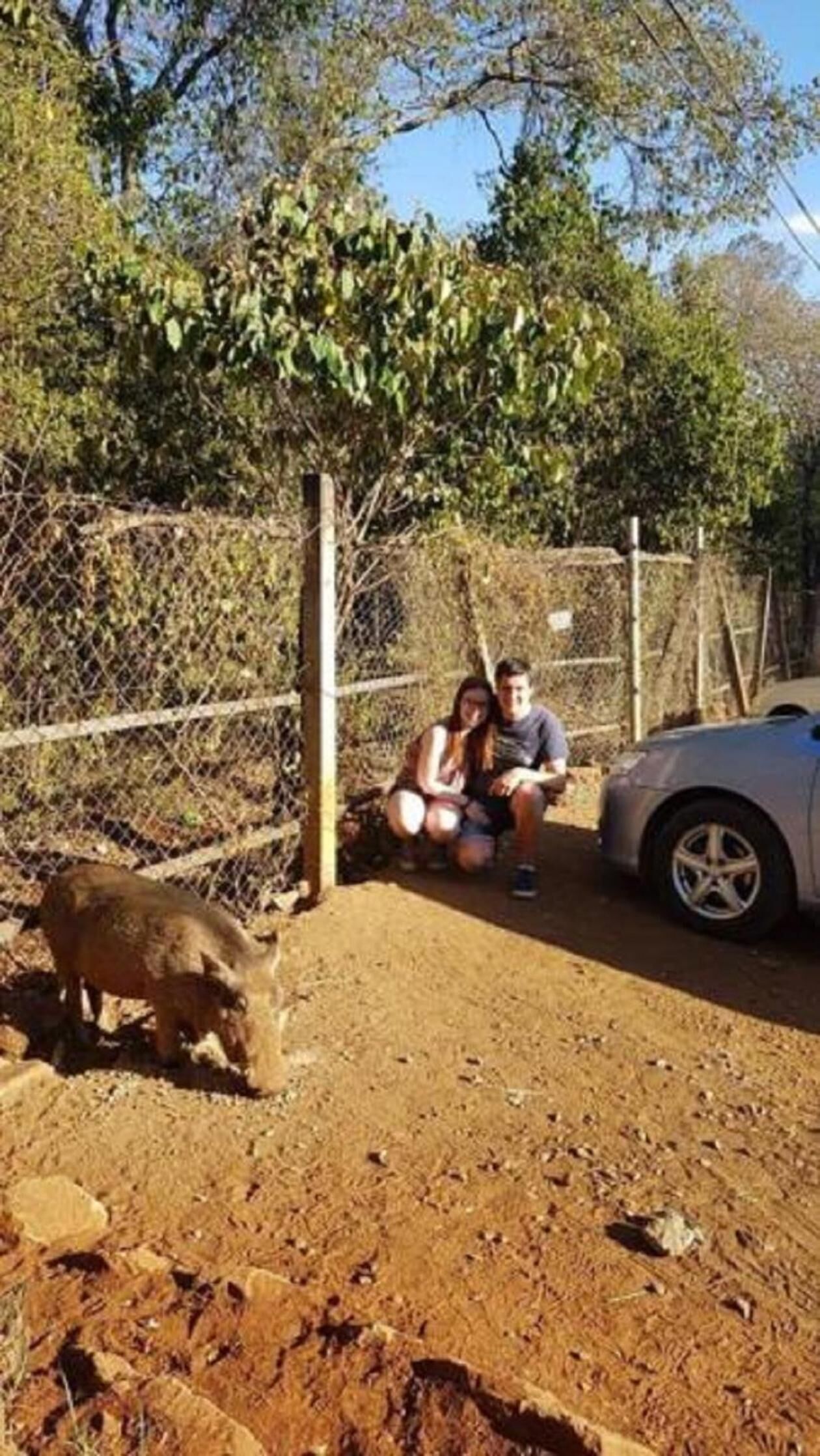 A fenced outdoor area with a dirt ground, a car, and a person sitting on a bench.