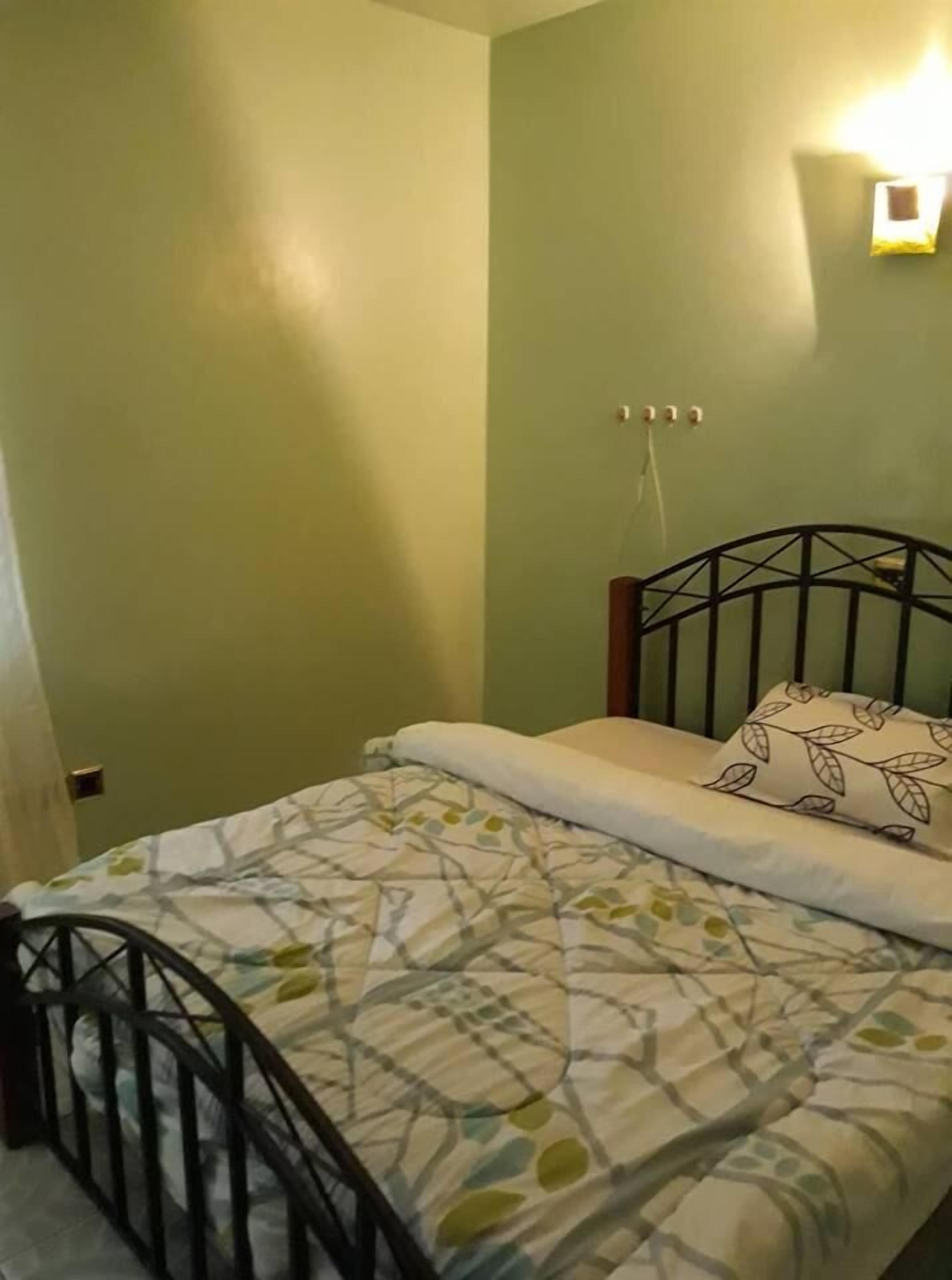 A single bed with a metal frame, a patterned bedspread, and a pillow with a leaf design.