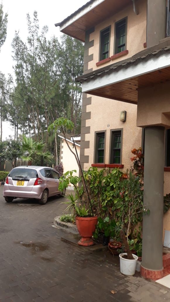 Edificio de dos pisos con un automóvil estacionado adelante. Hay plantas en macetas y un pequeño jardín.