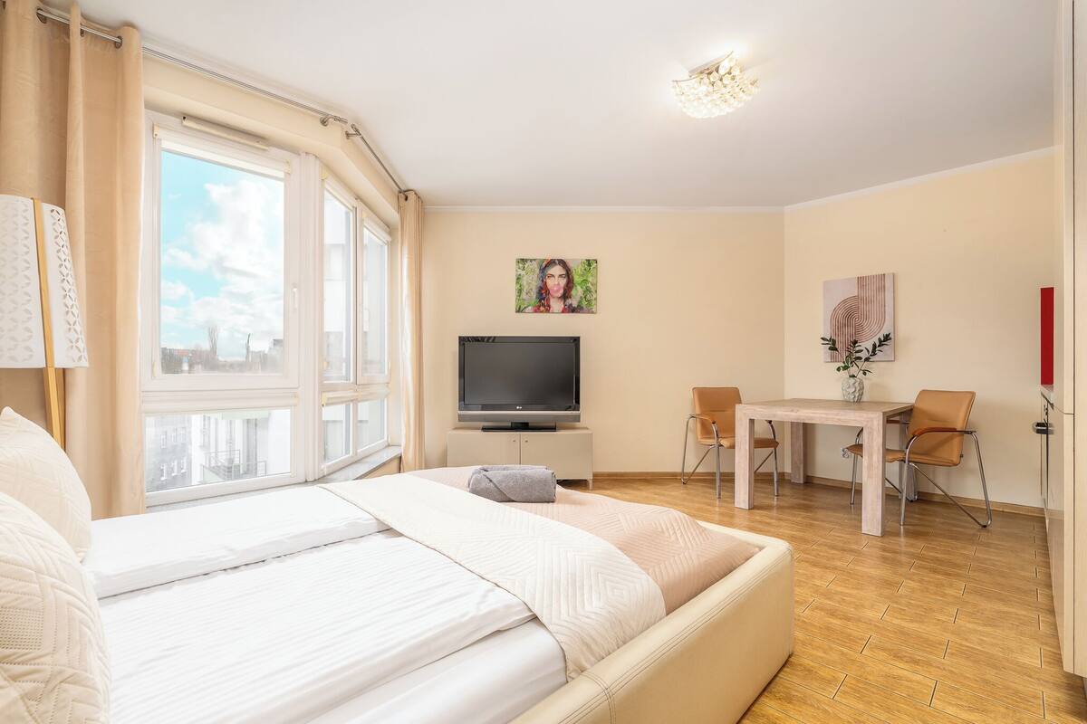 Habitació d'hotel amb llit, televisió, taula de menjador i cadires, i obra d'art a les parets.