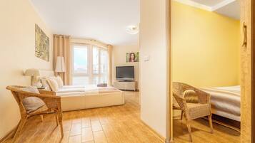 Una habitación acogedora con cama, un sofá, dos sillones de mimbre, un televisor y una ventana con cortinas.