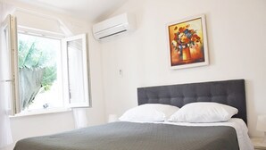 Un dormitorio con cama, ventana, aire acondicionado y un cuadro en la pared.