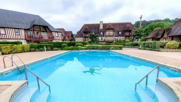 A swimming pool with a tiled deck, surrounded by traditional half-timbered houses.