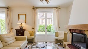 A living room with a sofa, armchairs, a glass coffee table, a fireplace, and a view through a glass door.