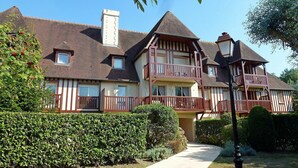 A large, two-story house with a balcony, surrounded by well-maintained hedges and a clear sky.