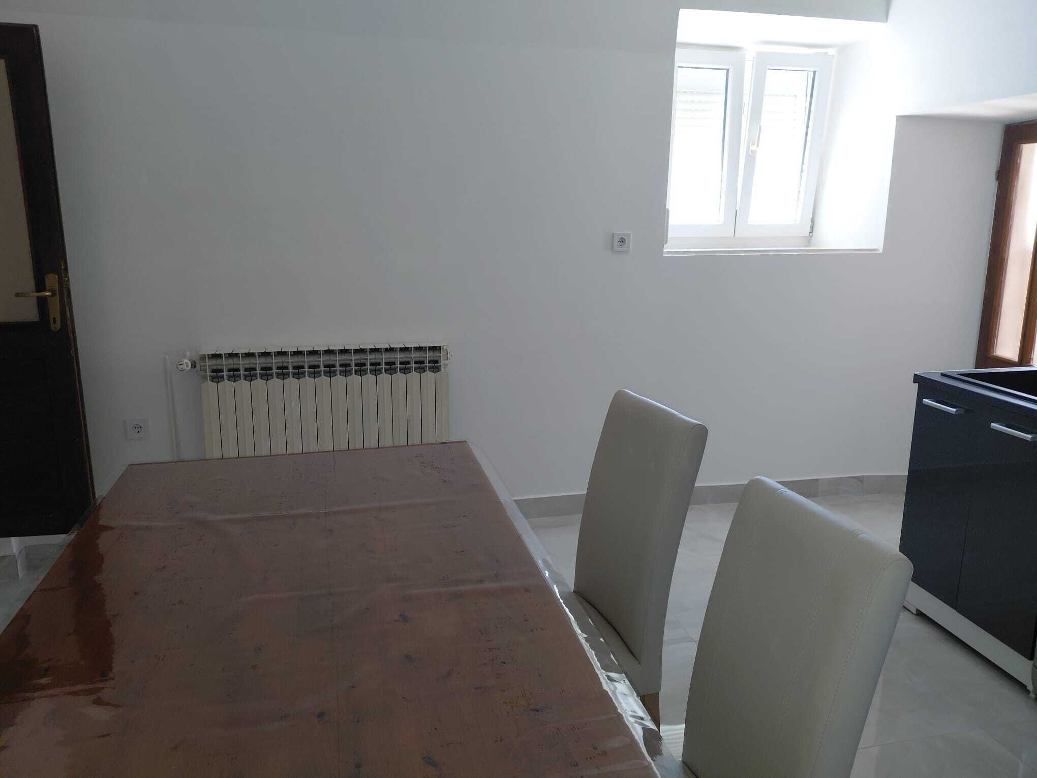 Une pièce comprenant une grande table, deux chaises, un radiateur, une fenêtre et un meuble de couleur sombre.
