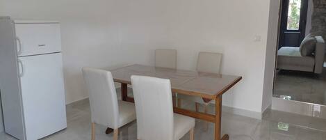 Un comedor con una mesa y cuatro sillas, un refrigerador blanco y una puerta que da a otra habitación.