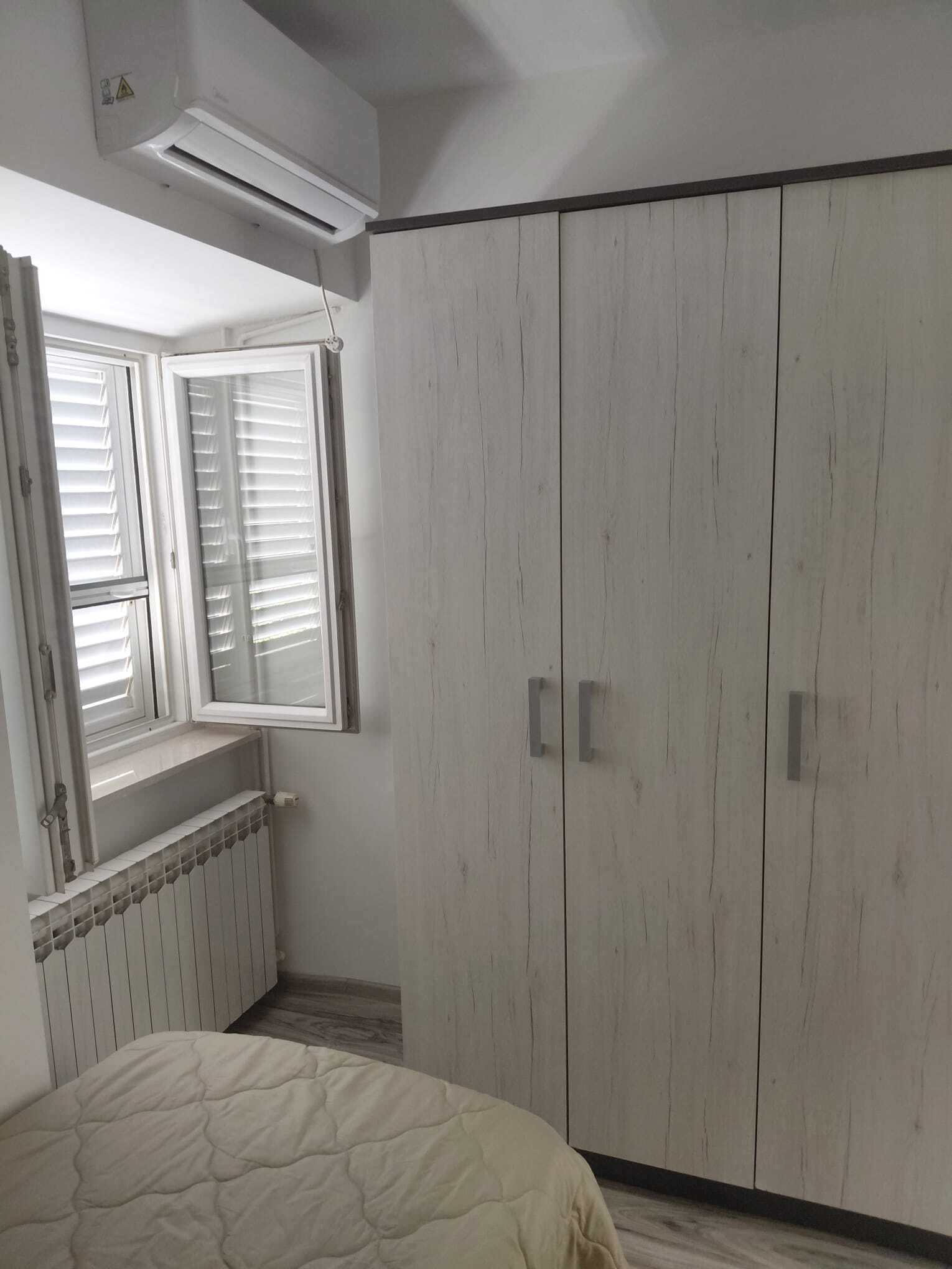 Een slaapkamer met een bed, een raam met zonwering, een radiator en een kledingkast.
