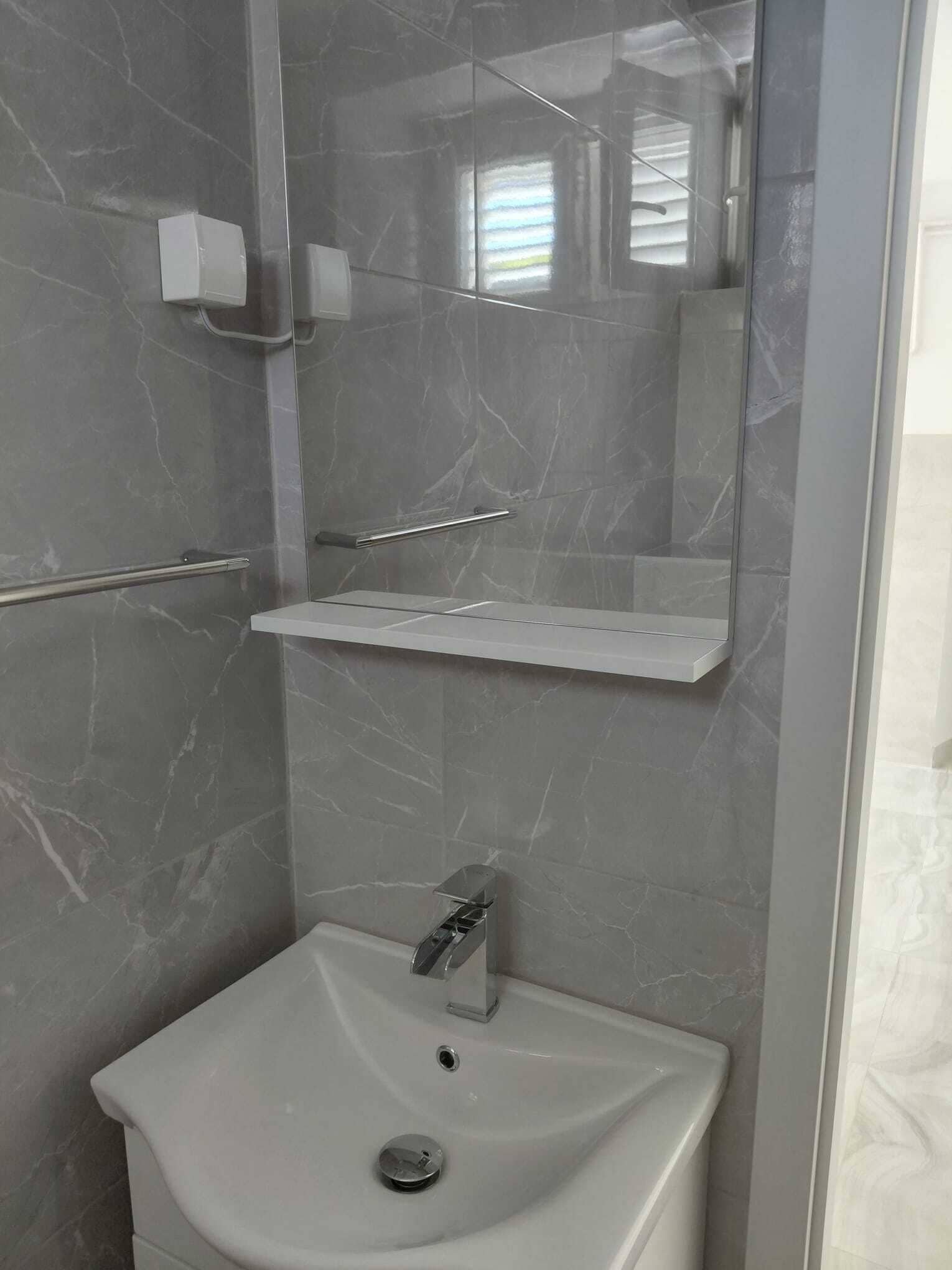 Un baño con pared de mármol, lavamanos blanco, espejo y cabina de ducha.