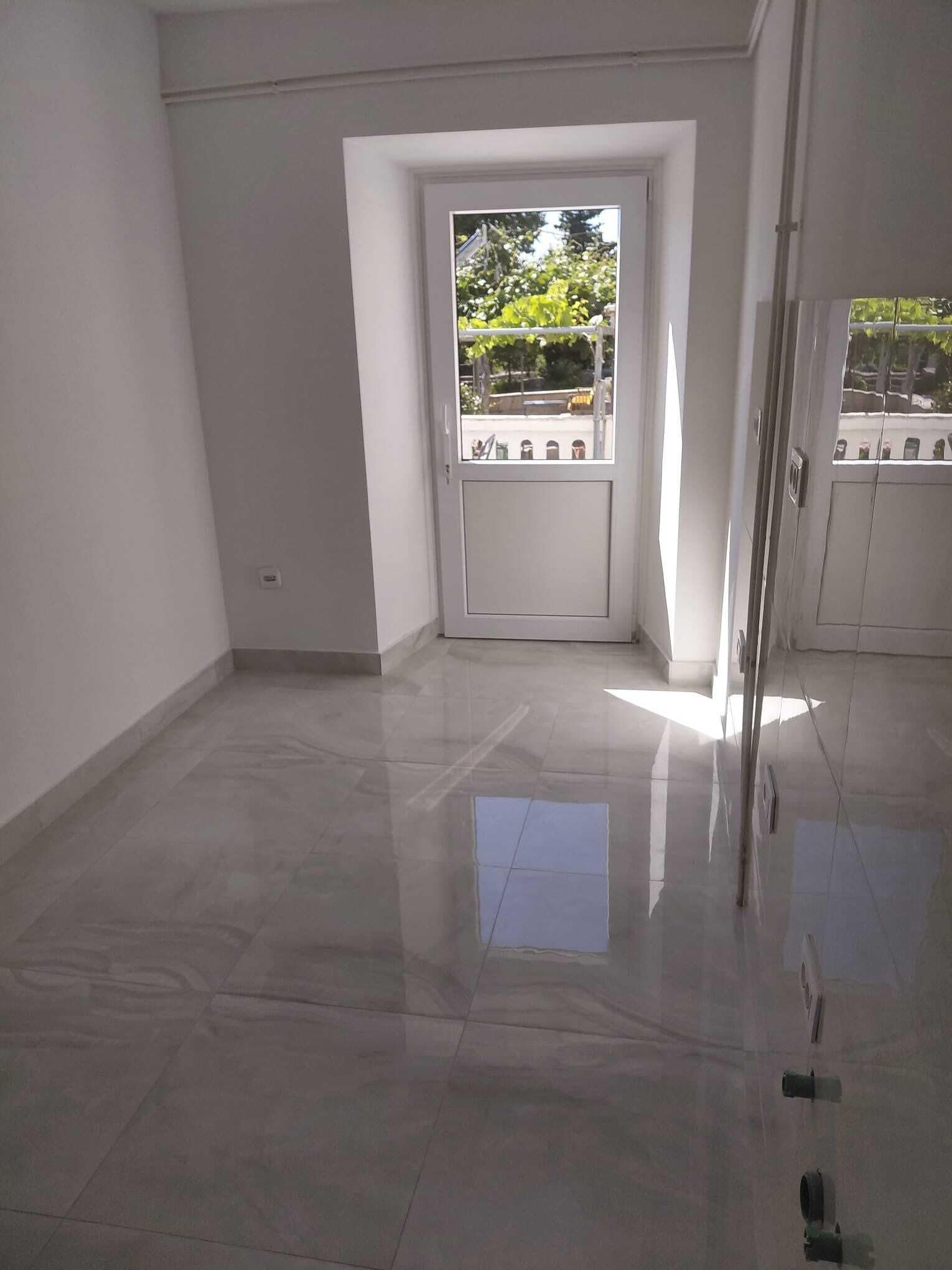 Una habitación con suelo de baldosas, una puerta blanca con ventanal y vistas al exterior con vegetación.
