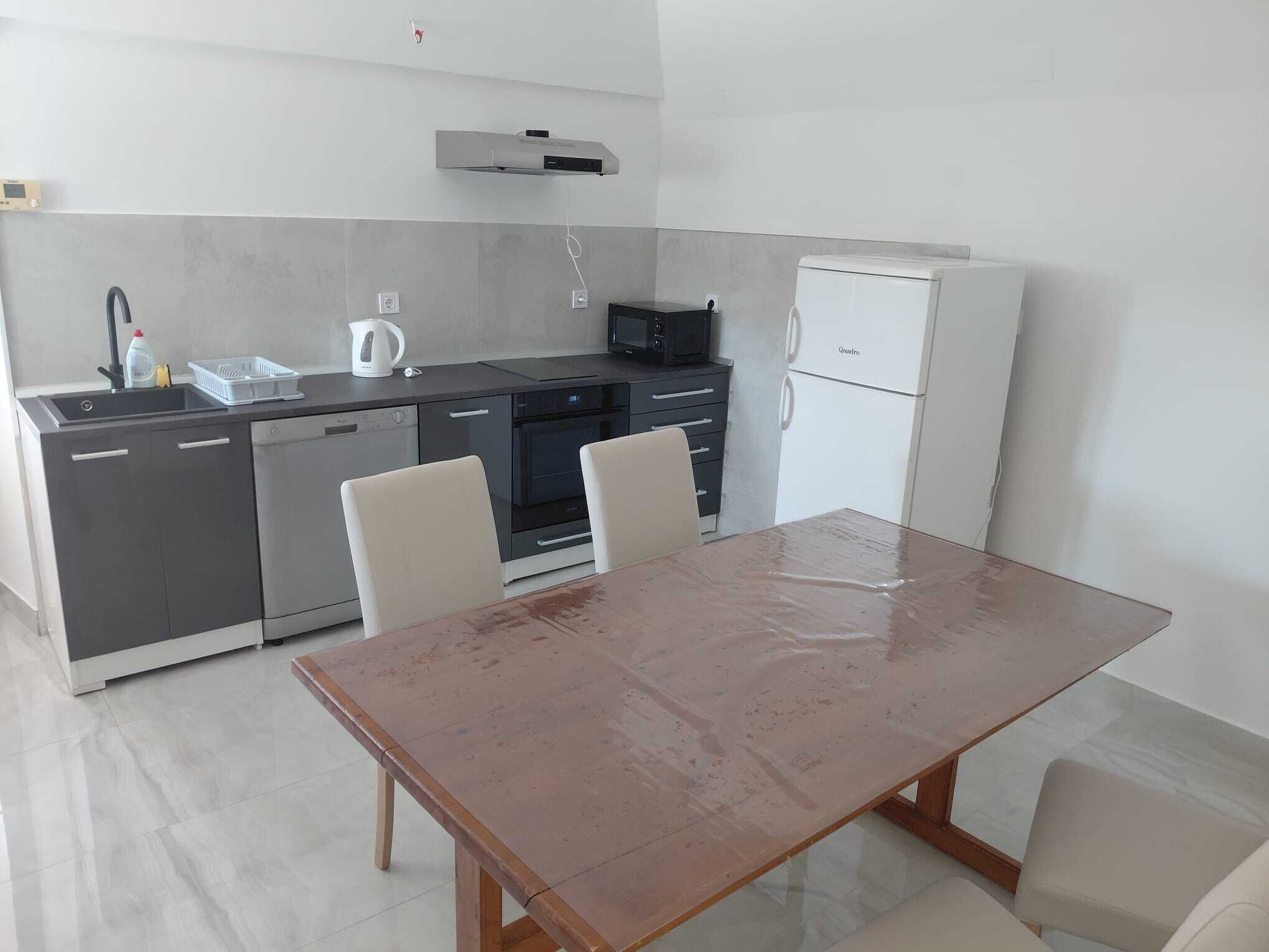 A compact kitchen with a dishwasher, oven, microwave, and refrigerator. There is a dining table with chairs.