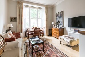 A well-lit living room with a sofa, coffee table, and a television. - The Hummingbird Apartment (London)
