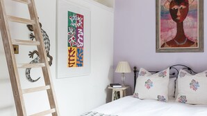 Une chambre à coucher comprenant un lit, une échelle, une table de chevet, une lampe et deux œuvres d’art accrochées au mur.