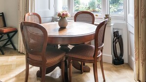 Une salle à manger avec une table ronde, quatre chaises, un vase de fleurs et une fenêtre avec des rideaux.