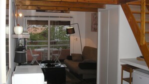 A cozy living room with a sofa, a coffee table, and a TV. There's a window with a view of trees and a lamp on a table. - HOLIDAY 'THE WATERFRONT' (Borgo)