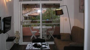 A living room with a sofa, a coffee table, a TV mounted on the wall, a floor lamp, and a sliding glass door leading to an outdoor area with a table and chairs. - HOLIDAY 'THE WATERFRONT' (Borgo)