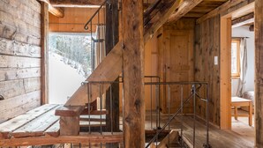 L’intérieur d’un chalet en bois, avec un escalier en bois, un banc et une vue sur un paysage enneigé.
