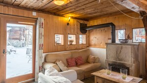L’intérieur d’un chalet accueillant, avec un plafond en bois, un canapé agrémenté de coussins, une table avec des verres et une cheminée.