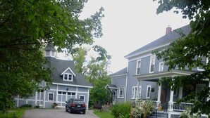 A residential street with houses on both sides, a parked car, and a driveway leading to a garage. - The Coach House (St. Stephen)