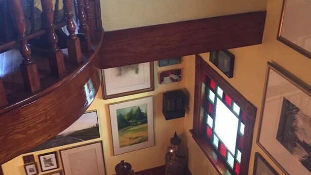 A wooden staircase with a view of the lower level, including a small statue and framed pictures on the walls. - The Coach House (St. Stephen)