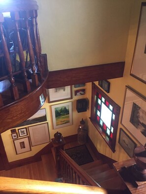 A wooden staircase with a view of the lower level, including a small statue and framed pictures on the walls. - The Coach House (St. Stephen)