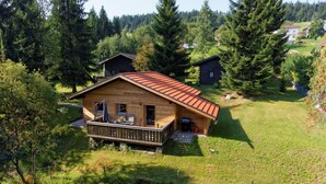 A wooden cabin with a balcony, surrounded by a grassy area and trees. - Ferienhaus Mitterdorf (Philippsreut)