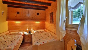 A cozy cabin room with two wooden beds, a small table with a lamp, and a window with curtains. - Ferienhaus Mitterdorf (Philippsreut)