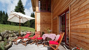 A wooden cabin with a deck, outdoor seating, and a table with a tablecloth. - Ferienhaus Mitterdorf (Philippsreut)