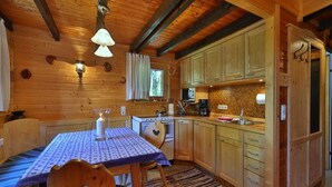 A cozy wooden cabin interior with a dining table, chairs, a kitchen area with wooden cabinets, a stove, and a microwave. - Ferienhaus Mitterdorf (Philippsreut)