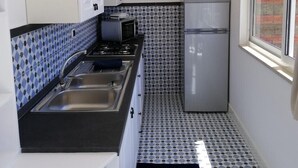 A compact kitchen with a gas stove, two sinks, a refrigerator, and a window providing a view of the outside. - Naples from a terrace - 6 (Napoli)
