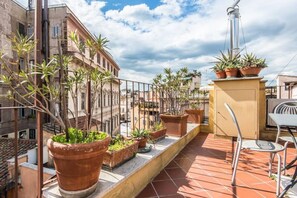 Een terras op het dak met terracotta potten, een metalen hekwerk en uitzicht op aangrenzende gebouwen.