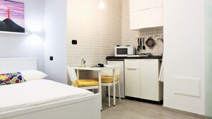 Una habitación pequeña con una cama, una mesa de comedor junto a una silla, un microondas y un lavabo.