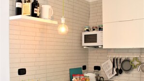 Cocina compacta con armarios blancos, un microondas blanco, un colgador de ollas y una mesa con cojines amarillos.
