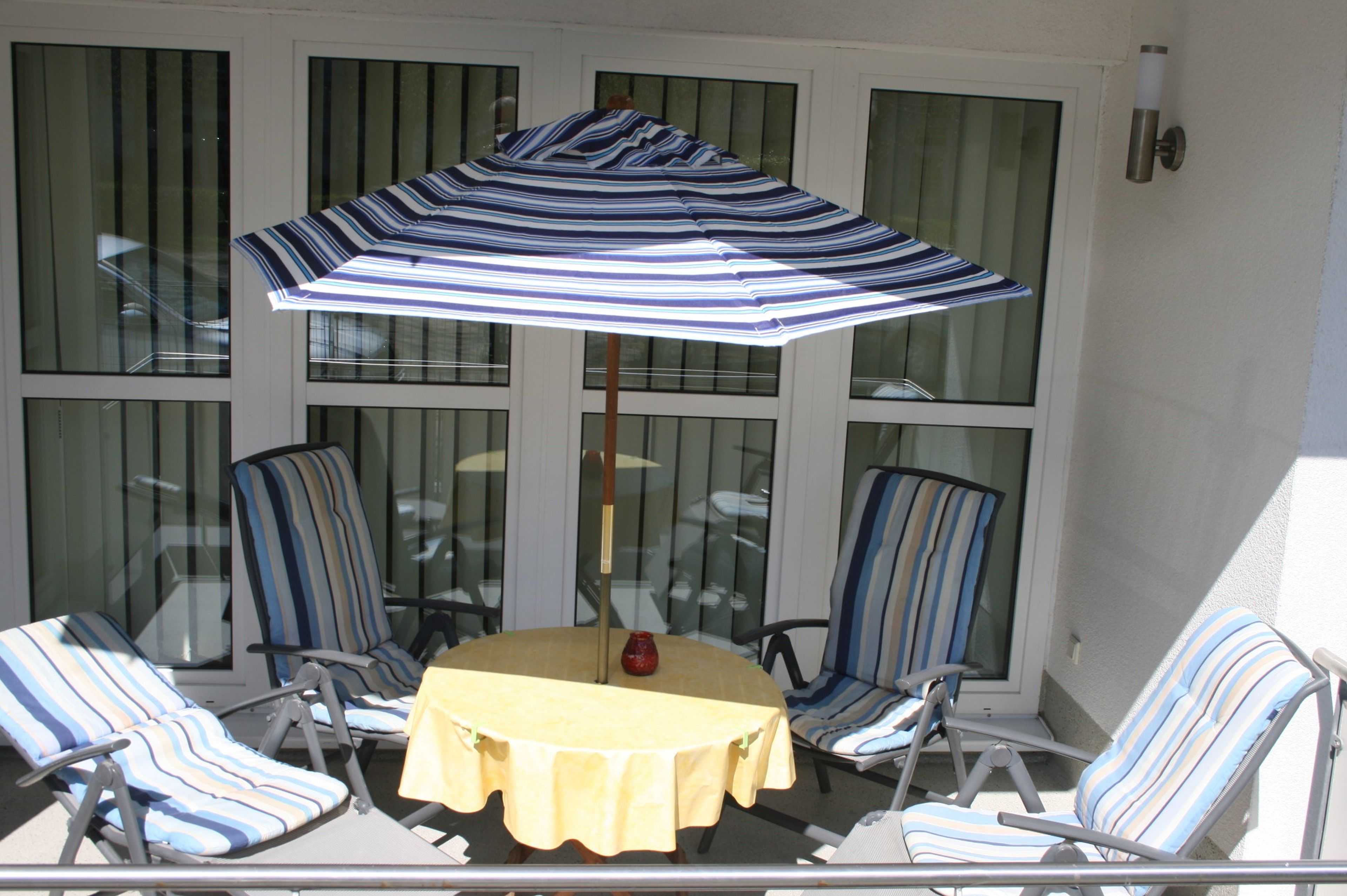 A sunlit patio with a round table, striped chairs, and a striped umbrella.